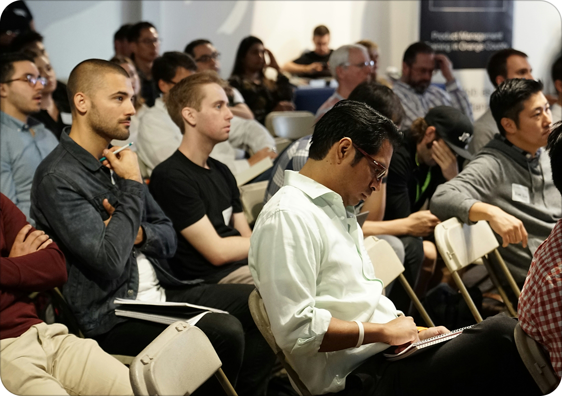 A diverse group of people attending a conference or seminar, sitting in rows and taking notes.