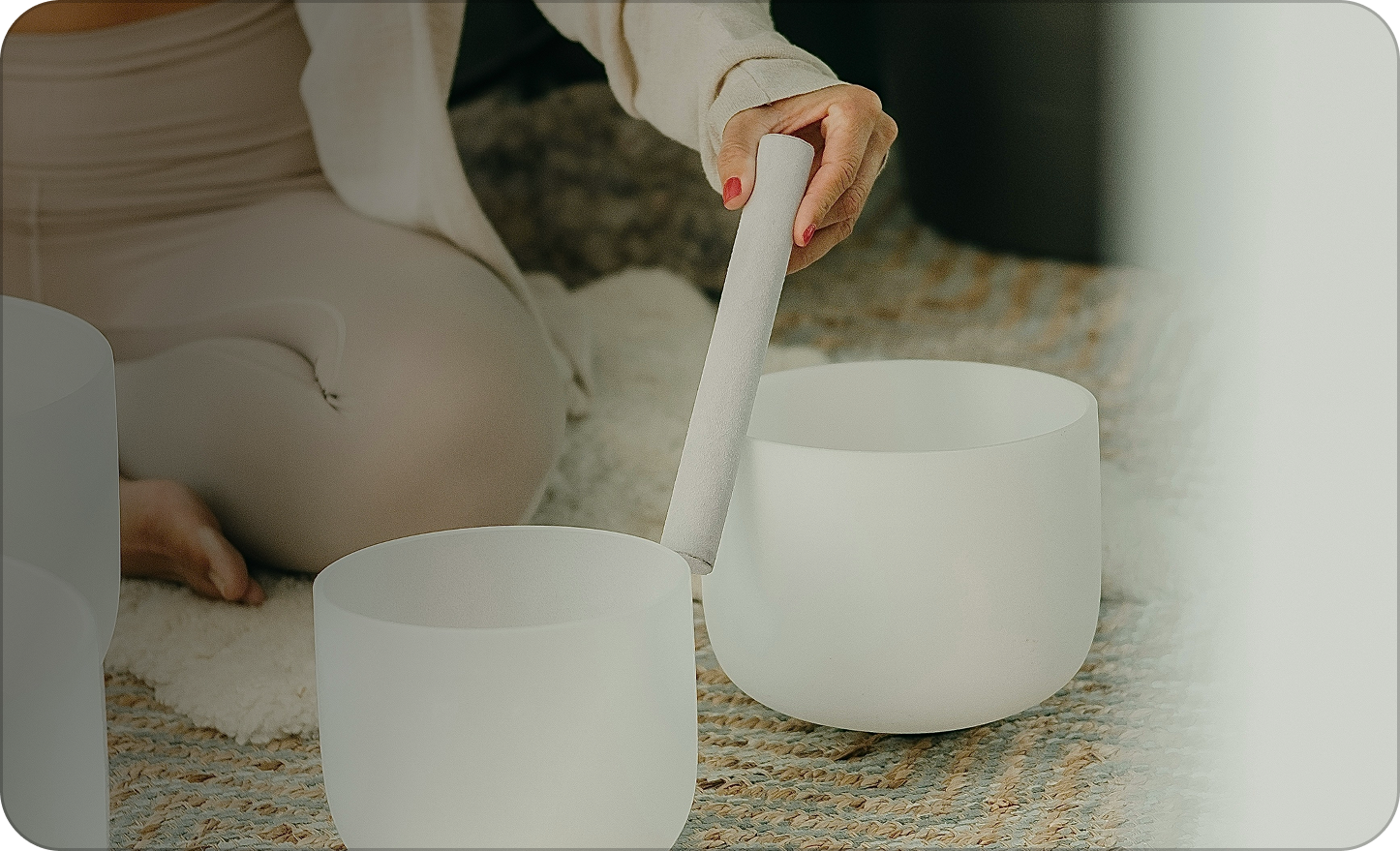 Person playing a crystal singing bowl with a mallet on a carpeted floor.