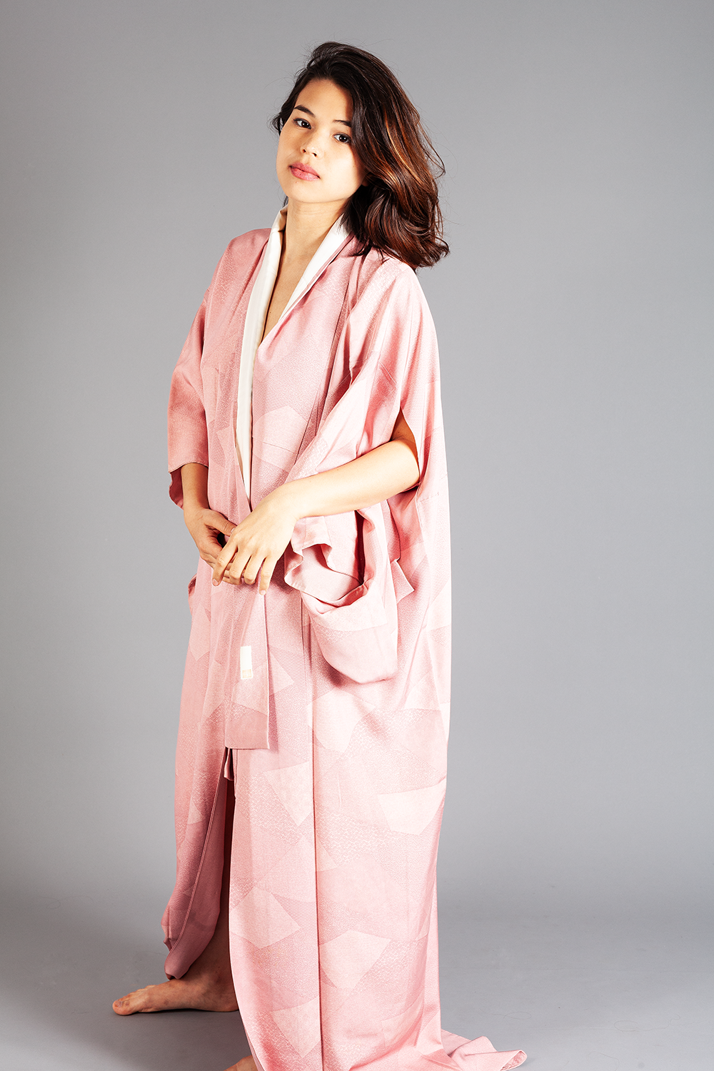 Junge Frau in traditionellem pinken Kimono vor grauem Hintergrund.
