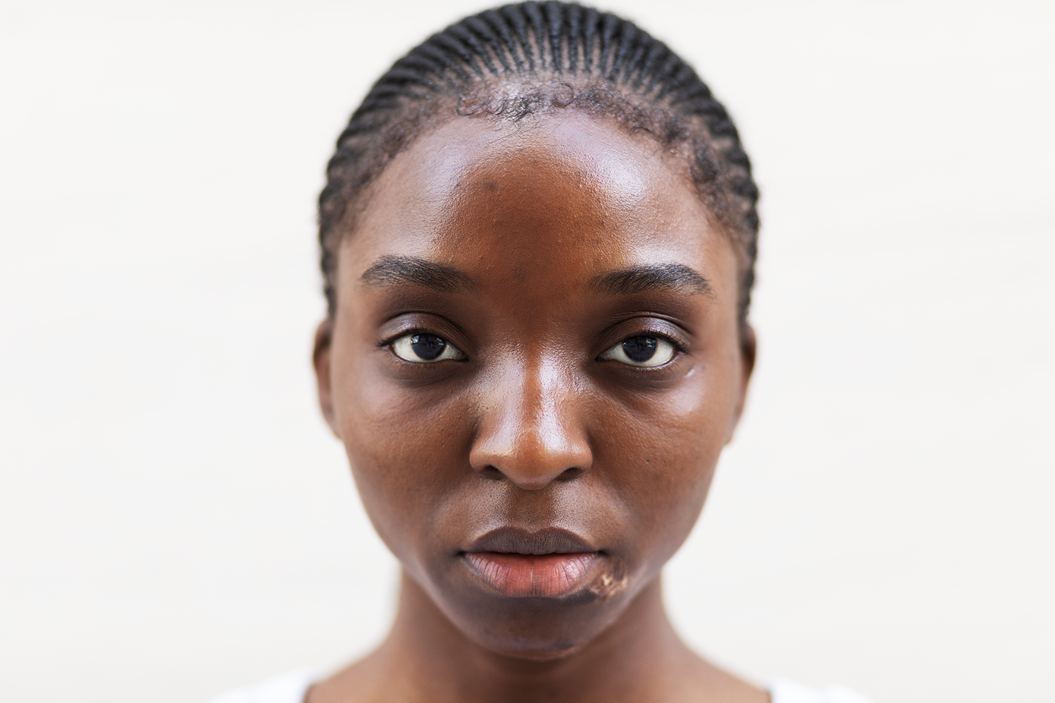 Nahaufnahme eines jungen schwarzen Mädchens mit natürlichen Haaren und ungetönter Haut, blickt direkt in die Kamera gegen einen weißen Hintergrund.