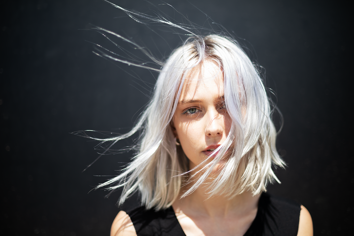 Porträt einer blonden Frau mit lockigem, zerzaustem Haar vor dunklem Hintergrund.