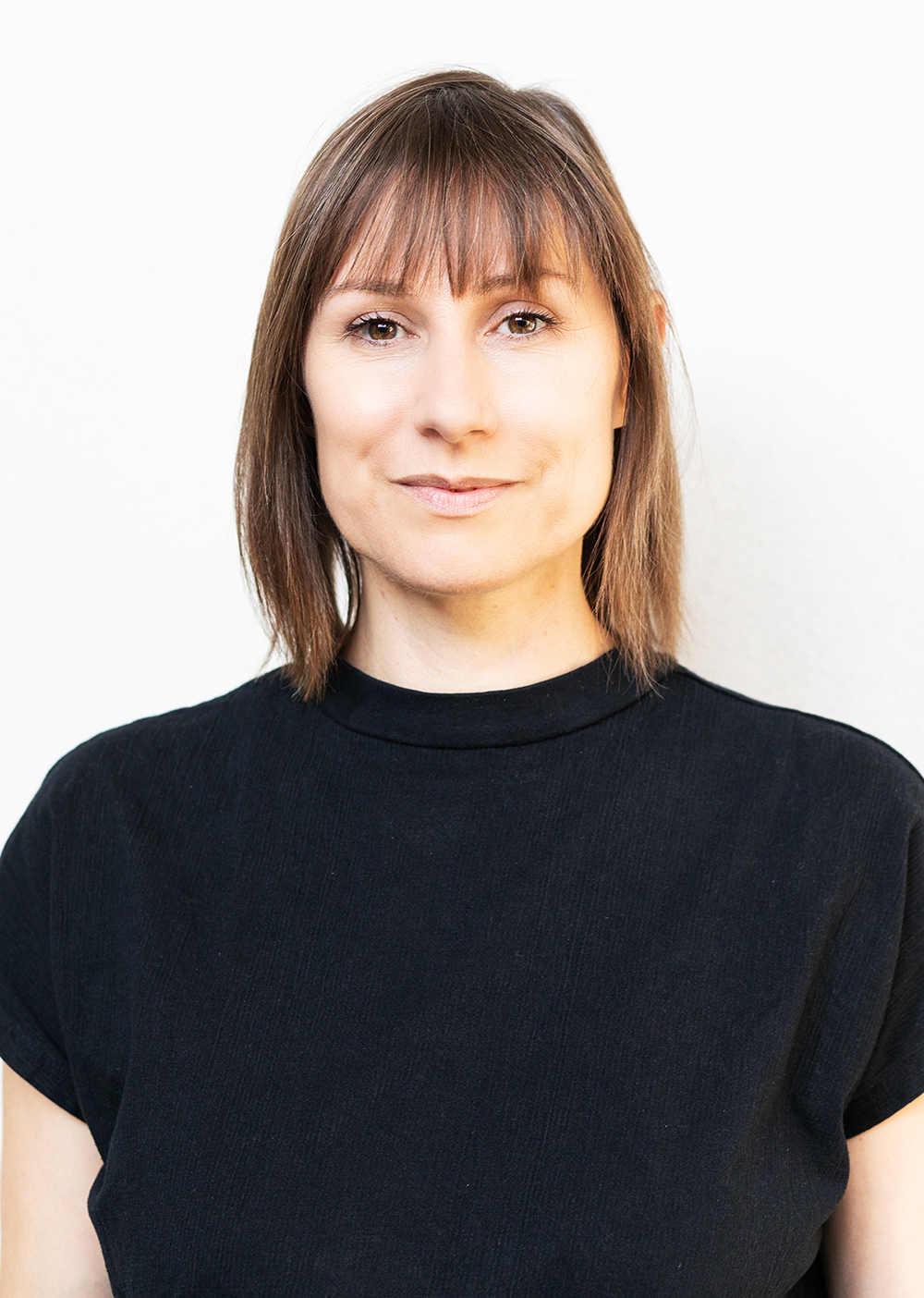 Porträt einer lächelnden Frau mit braunen Haaren und schwarzen T-Shirt vor weißem Hintergrund.