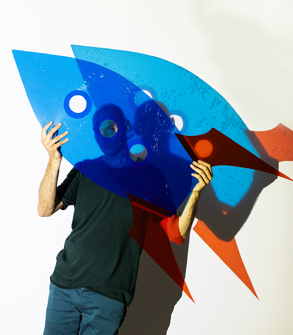 Person hält bunte, abstrakte Kunstinstallation vor Gesicht, Schatten an Wand