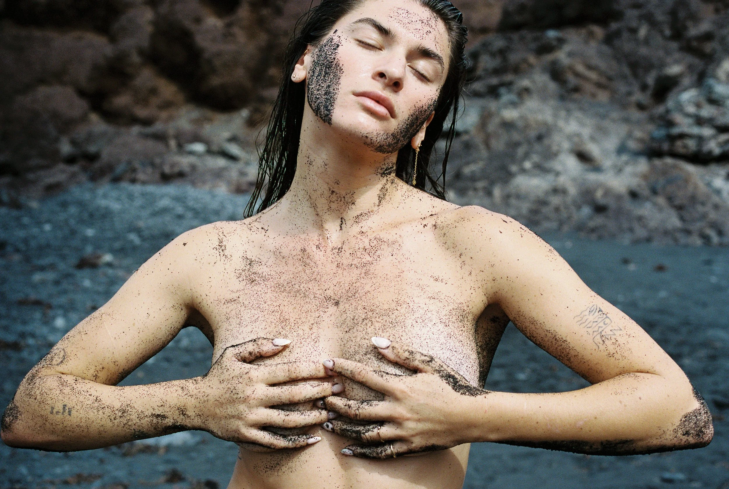 Photo of a female body showing her upper body torso, her breasts, her mouth. Photo taken in Lanzarote (Canary Islands) on a black sand beach. 
Film photo, 35mm Kodak Portra 400, Olympus OM-2. 