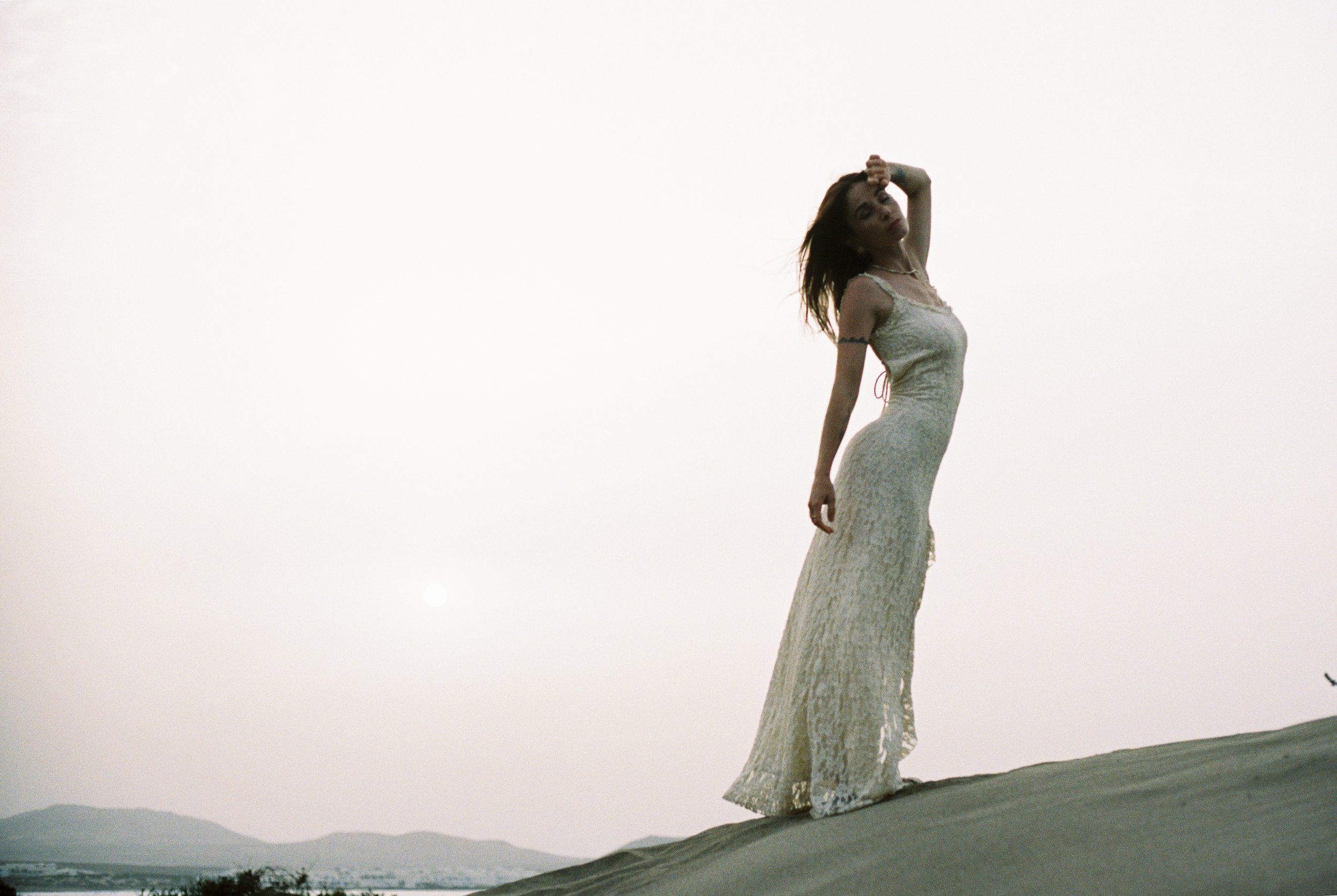 Photo of a female body showing her silhouette in a white dress. Photo taken backlight in Lanzarote (Canary Islands) on a white sand beach. 
Film photo, 35mm Kodak Portra 400, Olympus OM-2. 