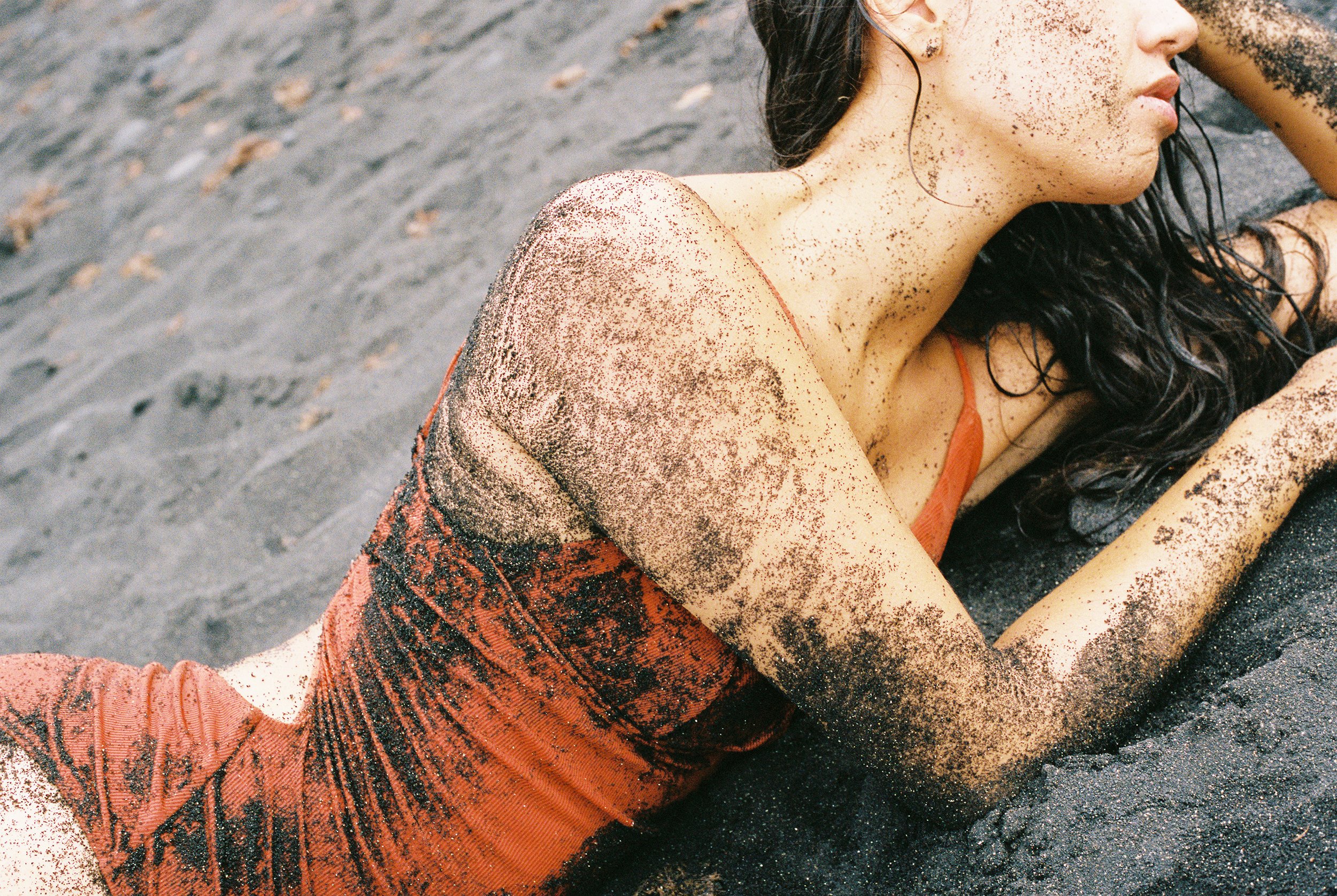 Photo of a female body showing her upper body torso, her mouth and her red bathing suit. Photo taken in Lanzarote (Canary Islands) on a black sand beach. 
Film photo, 35mm Kodak Portra 400, Olympus OM-2. 