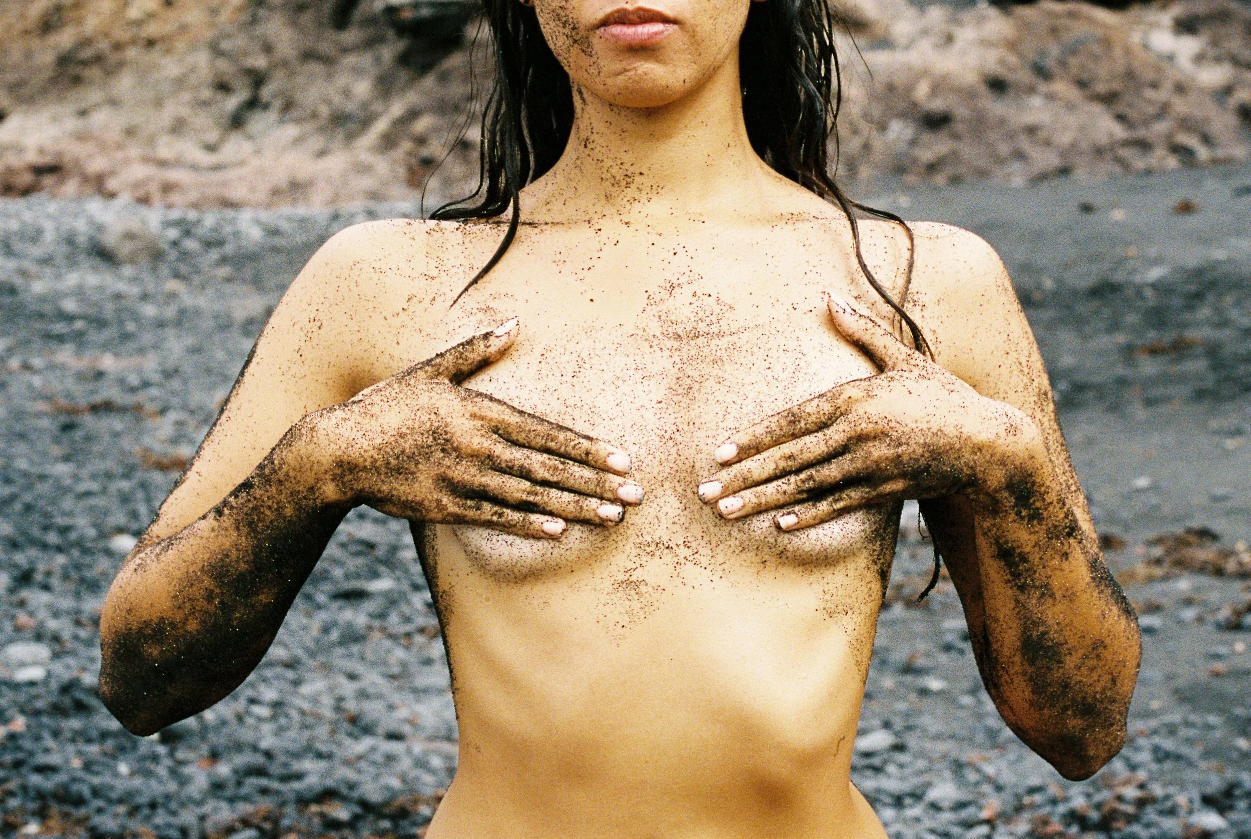 Photo of a female body showing her upper body torso, her breasts, her mouth. Photo taken in Lanzarote (Canary Islands) on a black sand beach. 
Film photo, 35mm Kodak Portra 400, Olympus OM-2. 