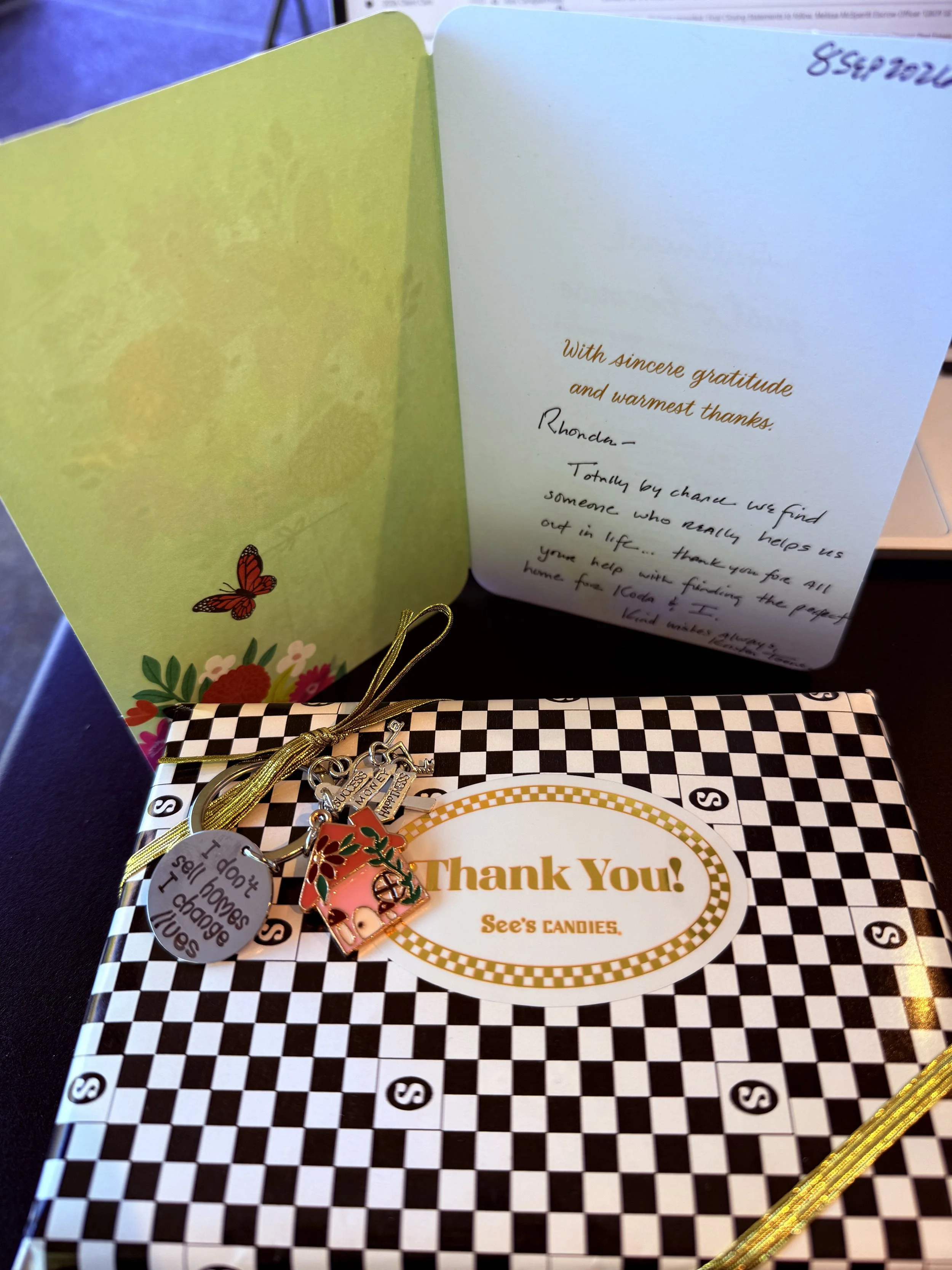 Handwritten thank-you card and a box of See's Candies with a gold ribbon and custom keychains, including one engraved with 'I don't sell homes, I change lives,' given by first-time homebuyer Kristen to Realtor Rhonda Riley in Oregon.