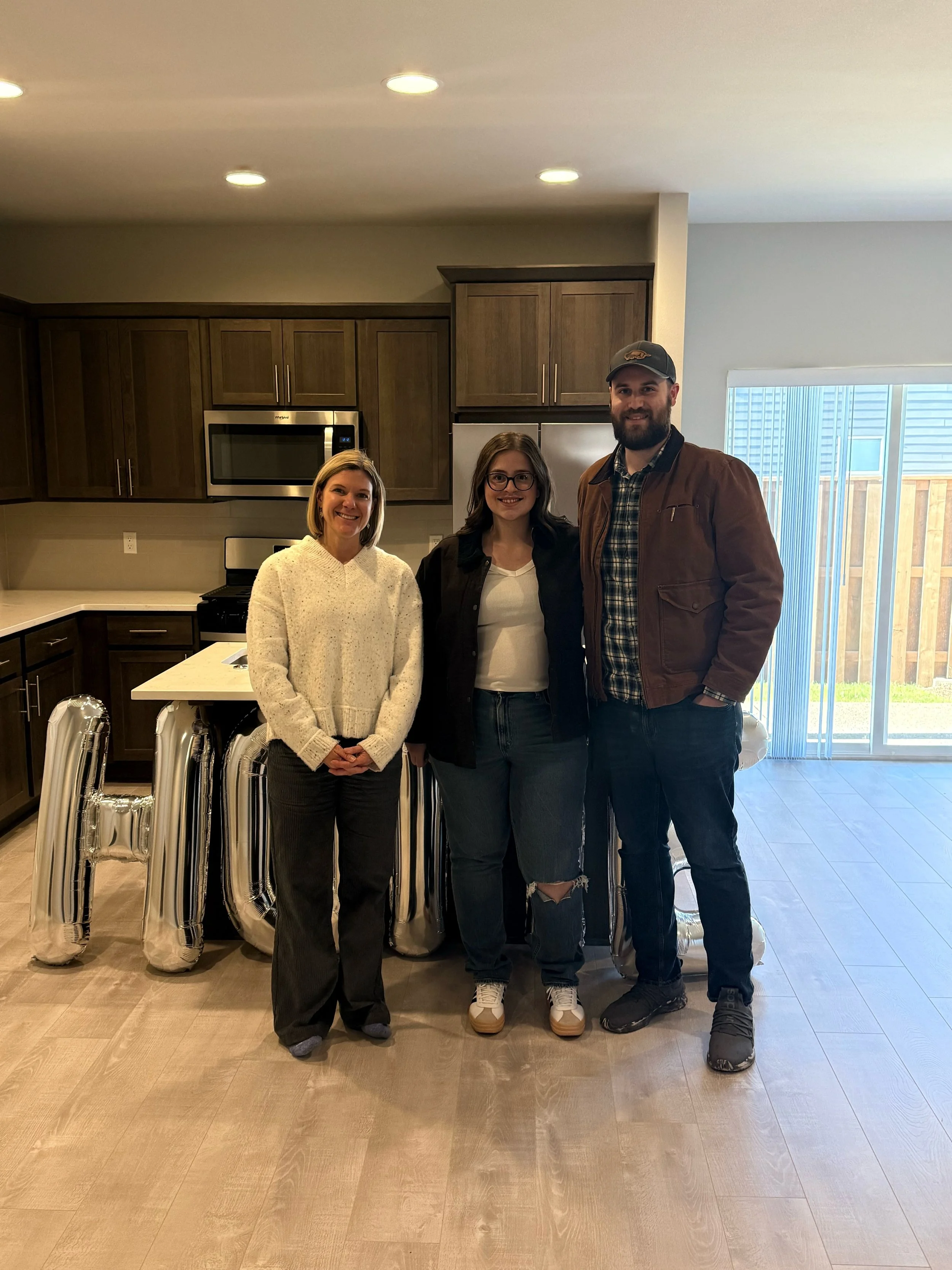Realtor Rhonda Riley and happy clients standing in a modern kitchen, a sliding glass door leading outside. Welcome Home, Key day.