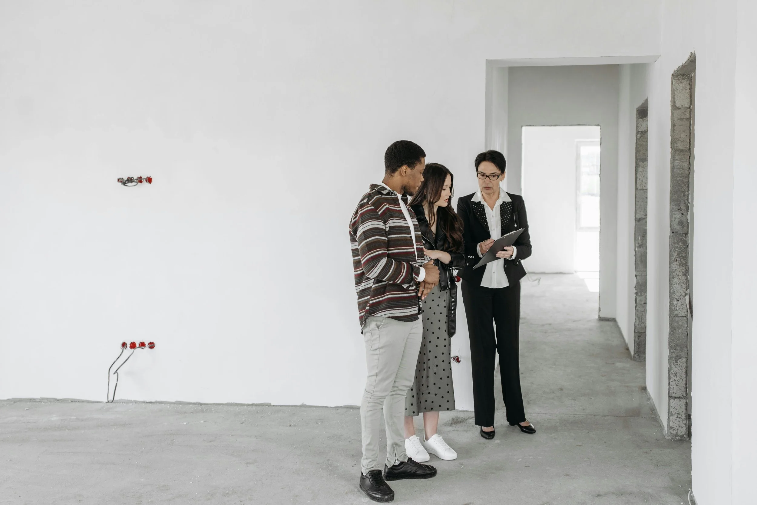 A real estate agent with a clipboard explaining construction details to a young couple inside an unfinished house in Forest Grove, Oregon.