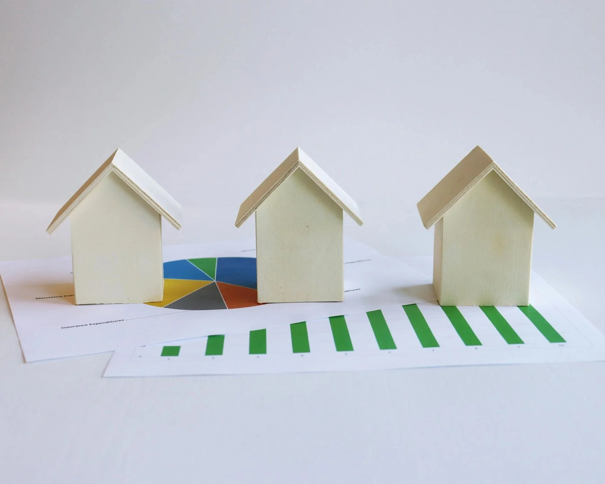 Three small wooden house models sitting on top of real estate market charts and financial growth graphs for Forest Grove, Oregon.