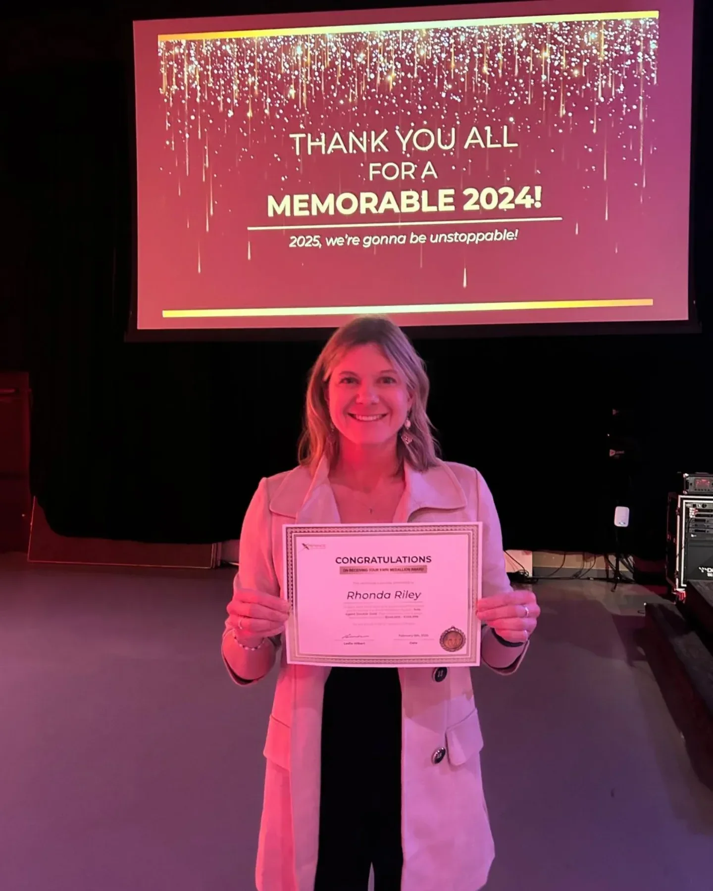 realtor rhonda riley smiling and holding a certificate on stage at an event,  gratitude and celebration.