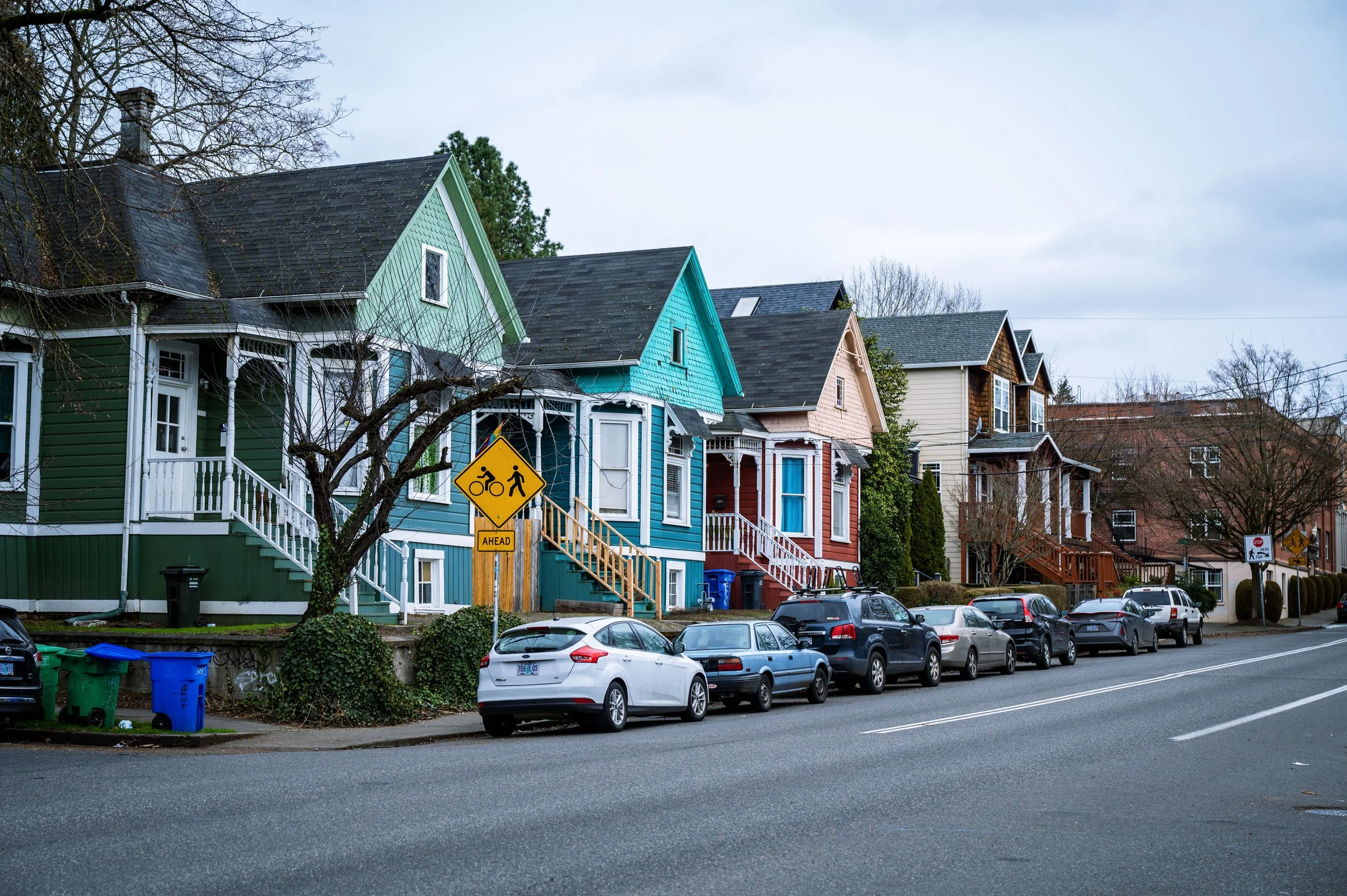 Row of colorful two-story residential homes along a street with parked cars in an Oregon neighborhood.