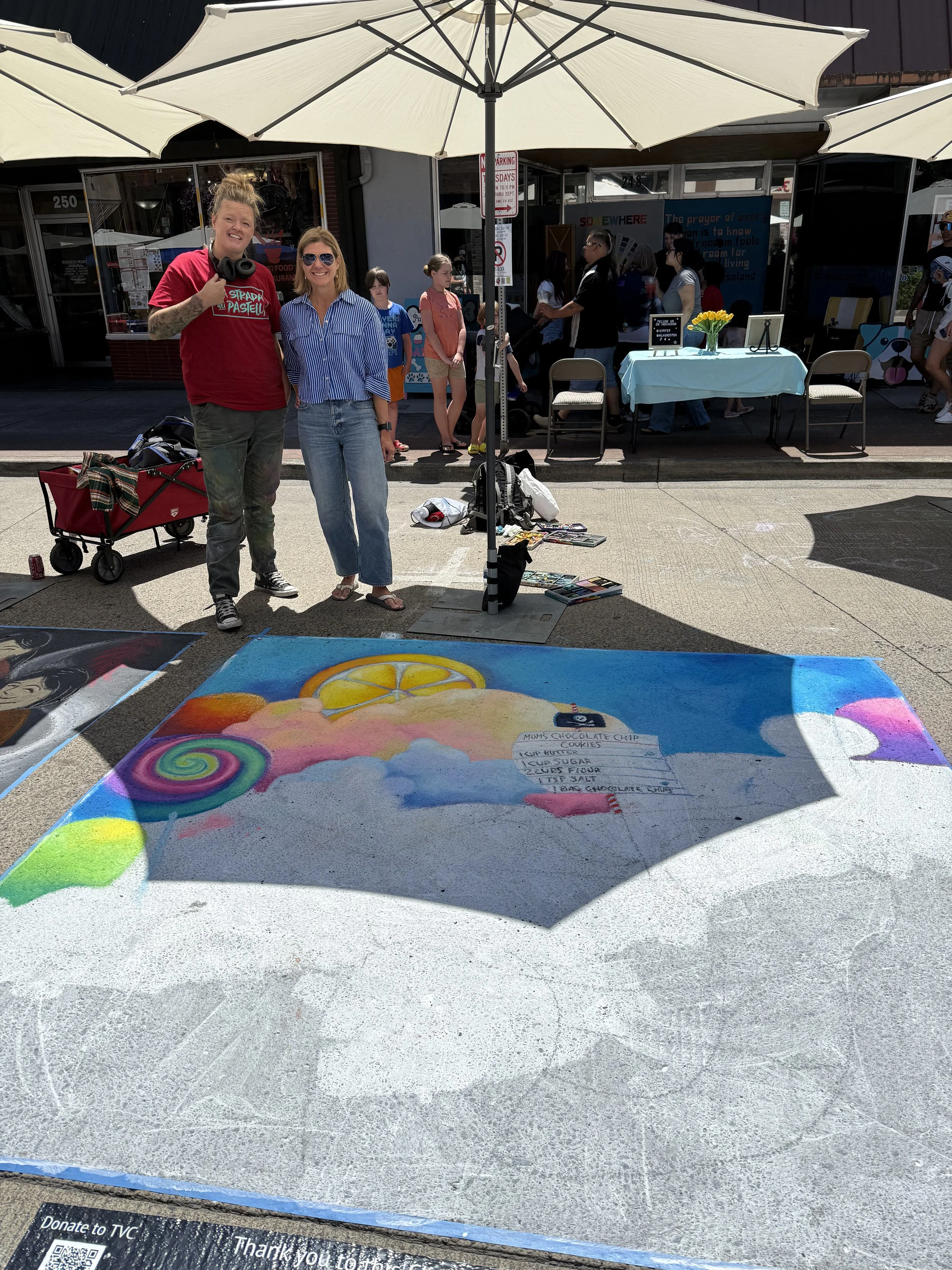 Chalk artist and Rhonda Riley smiling in front of a sponsored chalk art piece at Portland’s La Strada dei Pastelli Festival