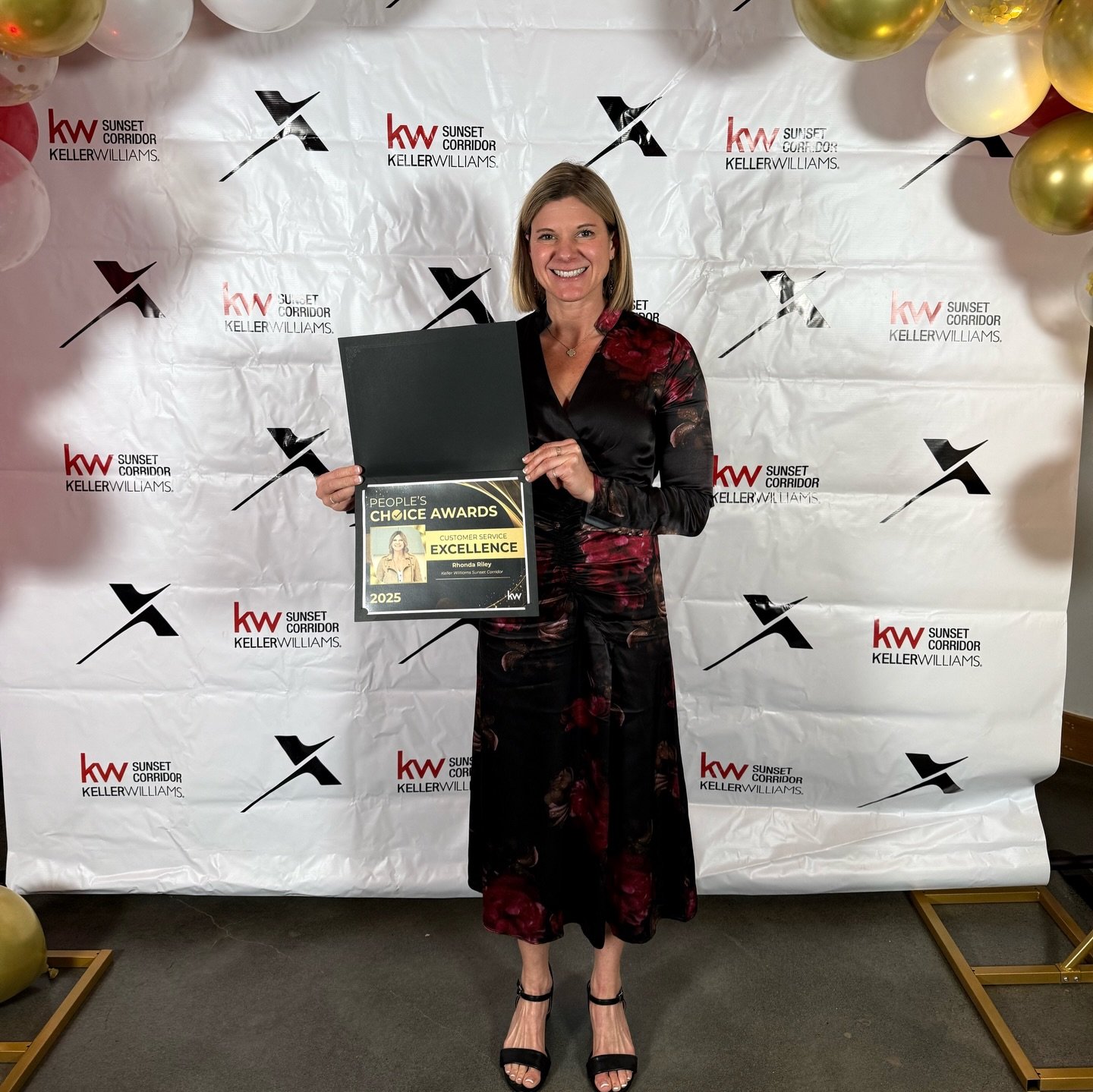 Rhonda Riley holding a certificate at an awards event, logos of Keller Williams and Sunset Corridor. Rhonda Riley is smiling, enthusiastic, caring for people.