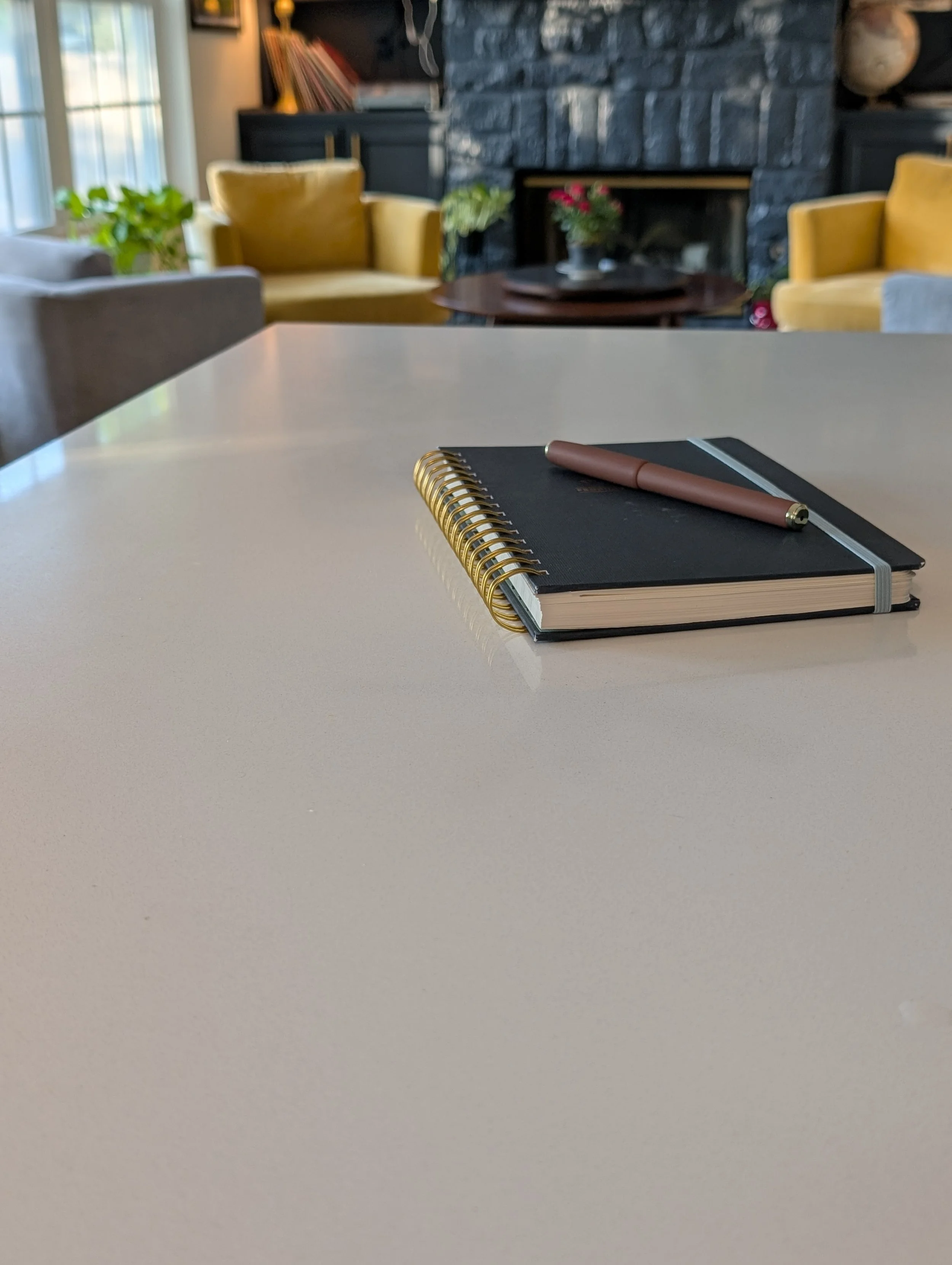 A navy spiral notebook and pen on a clean white surface with a cozy living area in the background, representing a focused start to micro-habit changes.