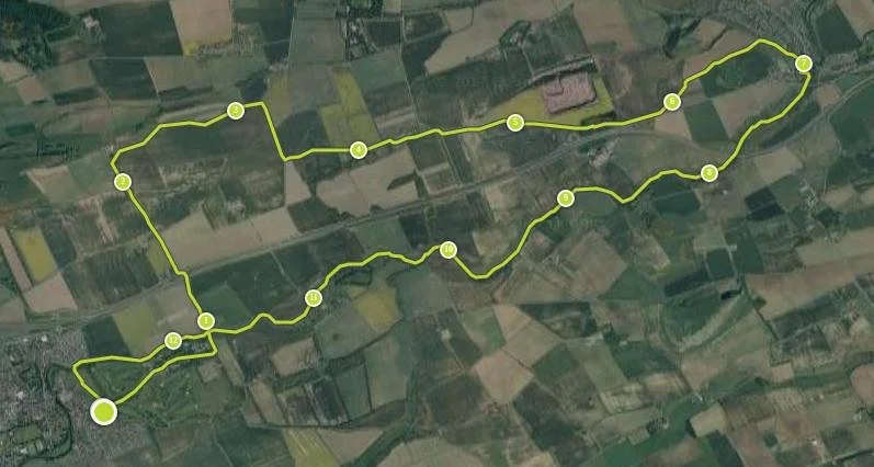 Satellite map showing a winding trail marked by yellow dots, over a green landscape with fields and farmland.