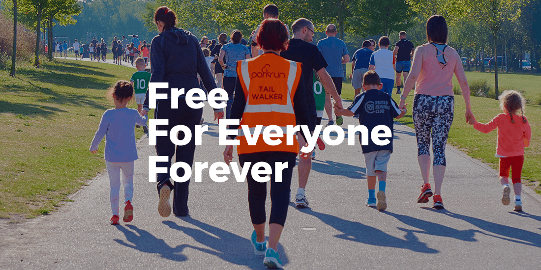 People participating in parkrun, a community walk or run event in a park, with a mix of adults and children, some holding hands.