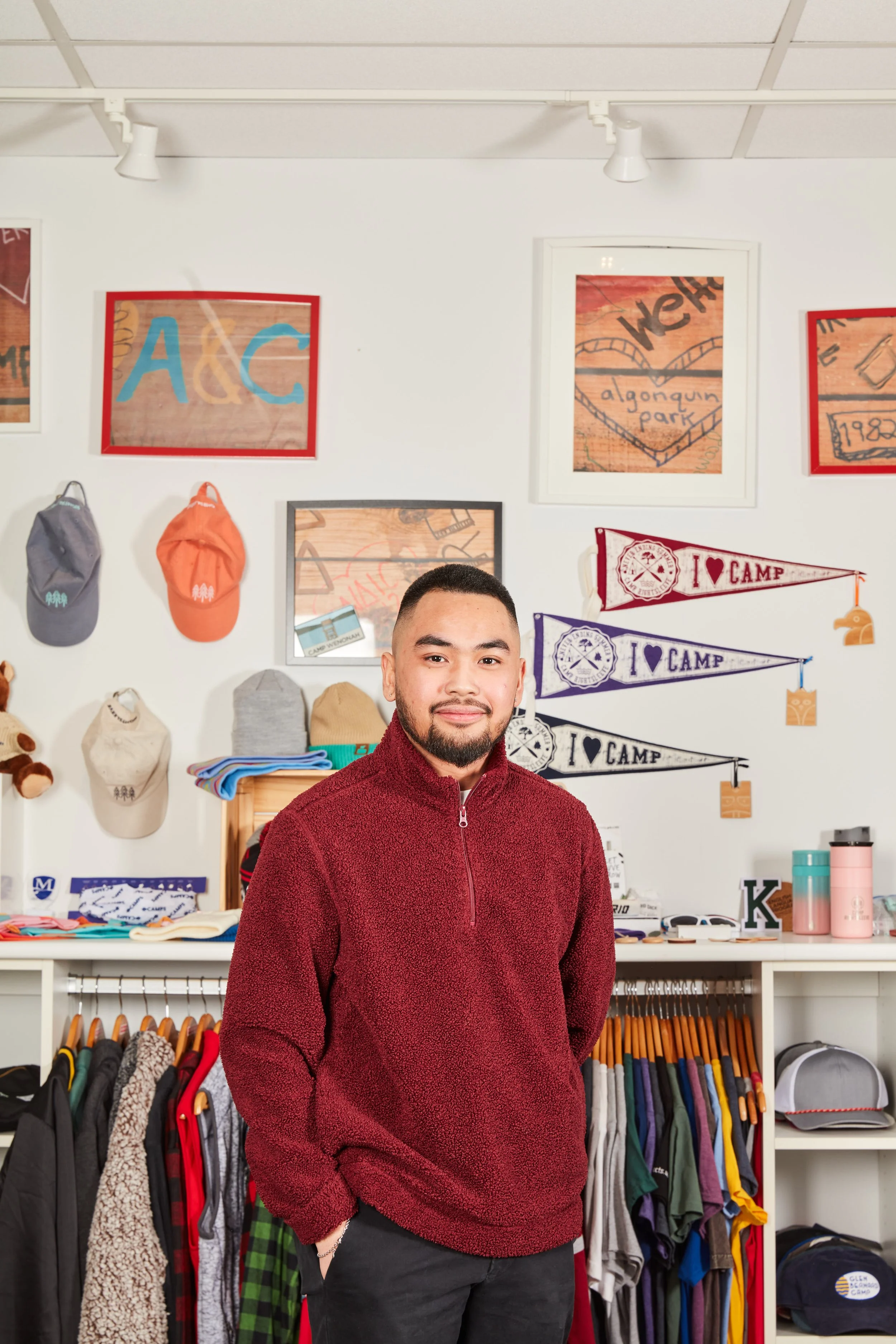 Miguel Castanos standing inside Project 116 showroom surrounded by custom branded merchandise including apparel, hats, and promotional products in Hamilton, Canada.