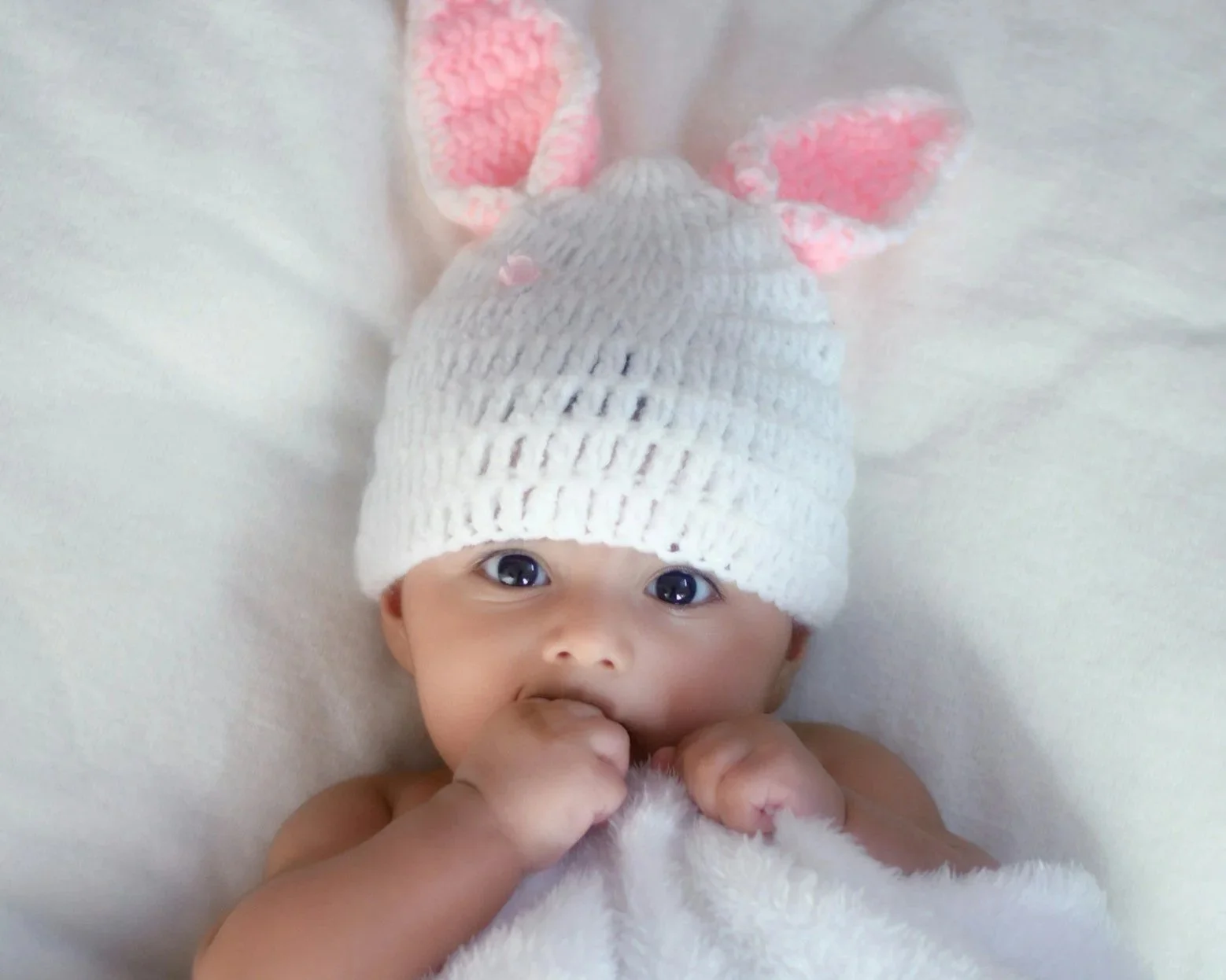 Infant baby wearing a knitted bunny ears hat while lying on back..