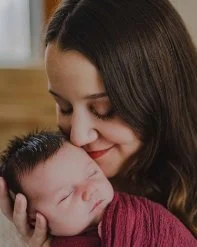 A woman gently holding and smiling at a sleeping baby.