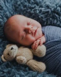 A sleeping newborn baby resting with a small stuffed teddy bear