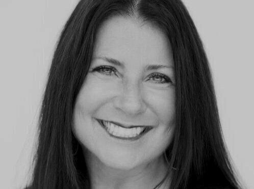 Black and white portrait of a smiling woman with long dark hair, showing her teeth, against a plain light background.