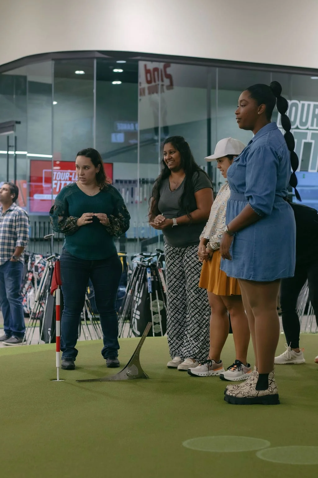 Group of four women standing on a miniature golf course, preparing to putt, at an indoor facility.