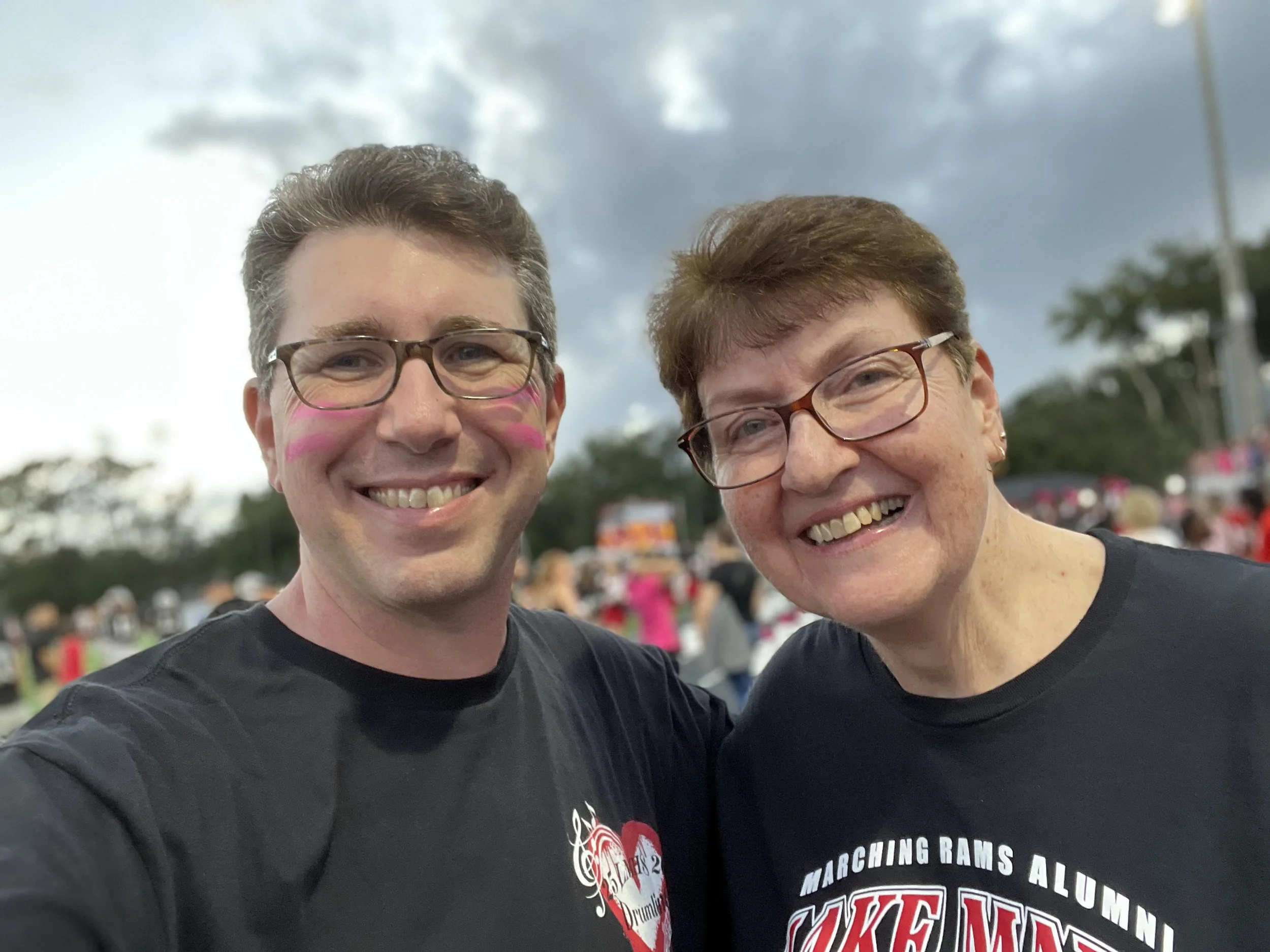 A man with glasses smiling at the camera, wearing a gray polo shirt with the Lake Mary logo and carrying a backpack.