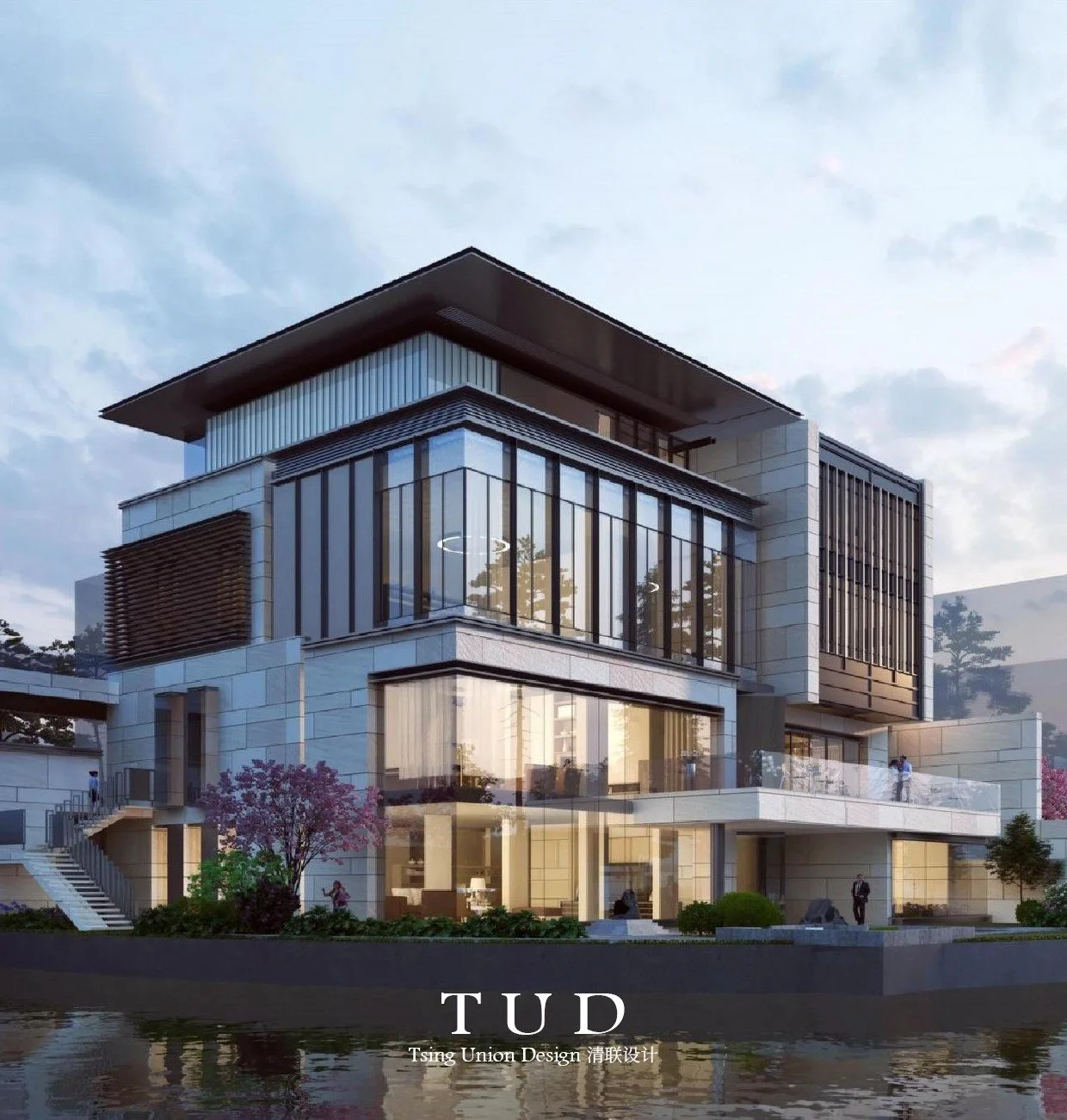Modern multi-story building with large glass windows, situated near a body of water, surrounded by trees and people walking around. The sky is partly cloudy.