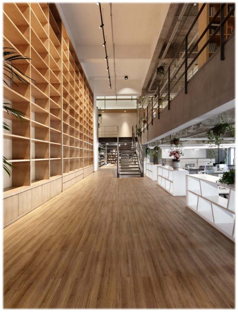 Interior of a modern, spacious bookstore or library with wooden shelves on the left, white display counters on the right, and a staircase leading to an upper level in the background.
