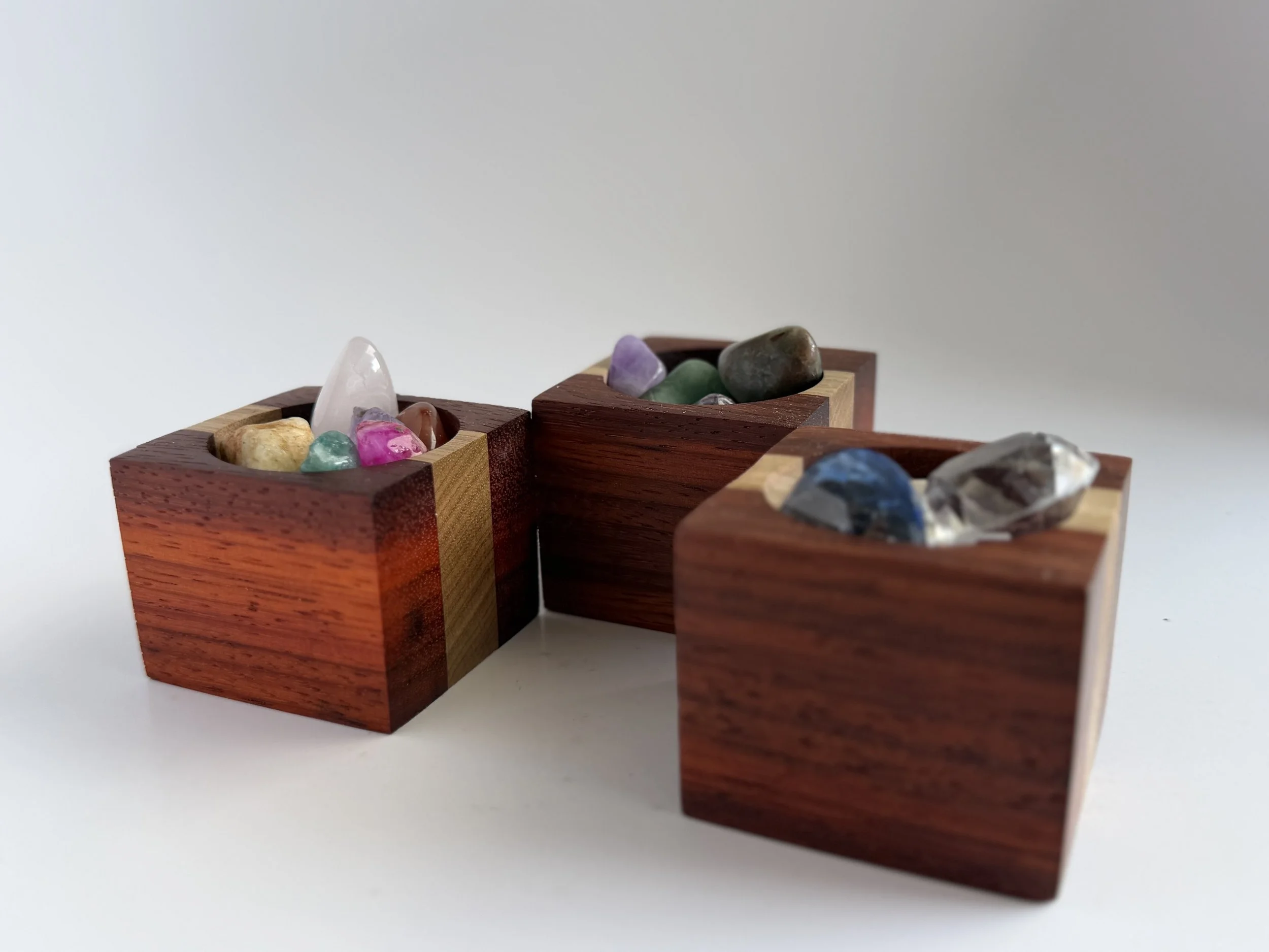 Three wooden boxes filled with colorful gemstones, placed on a white surface.