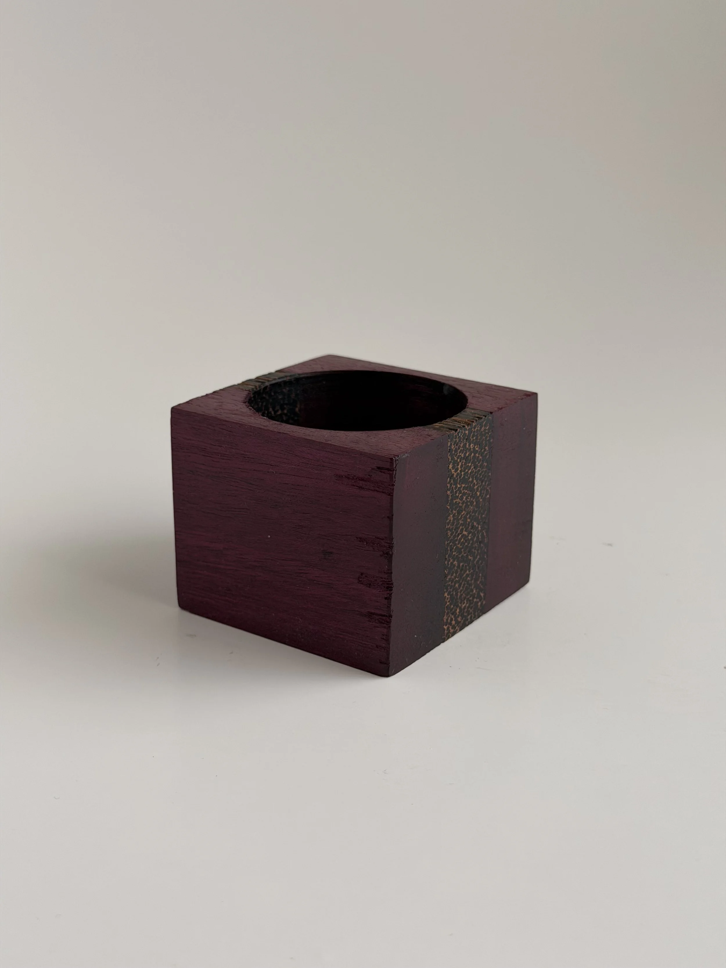 A small, dark red wooden box with a circular opening on top, placed on a plain white background.