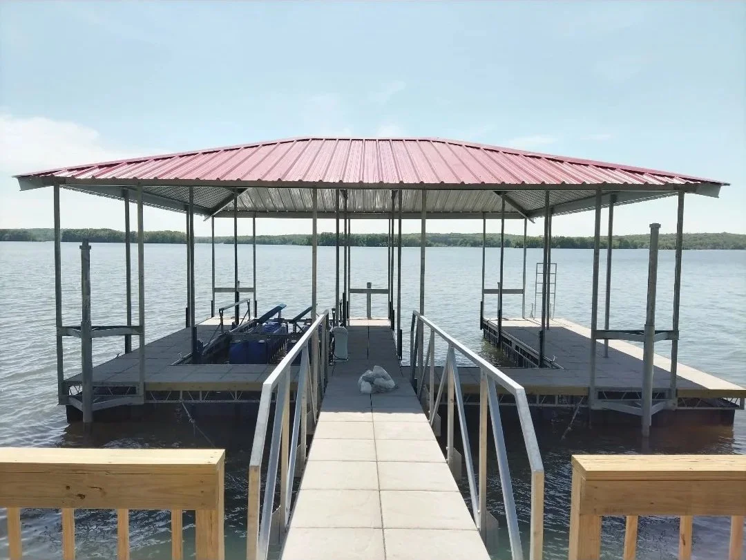 A boat dock with a metal roof extending over the water, connected by a concrete walkway with railings.