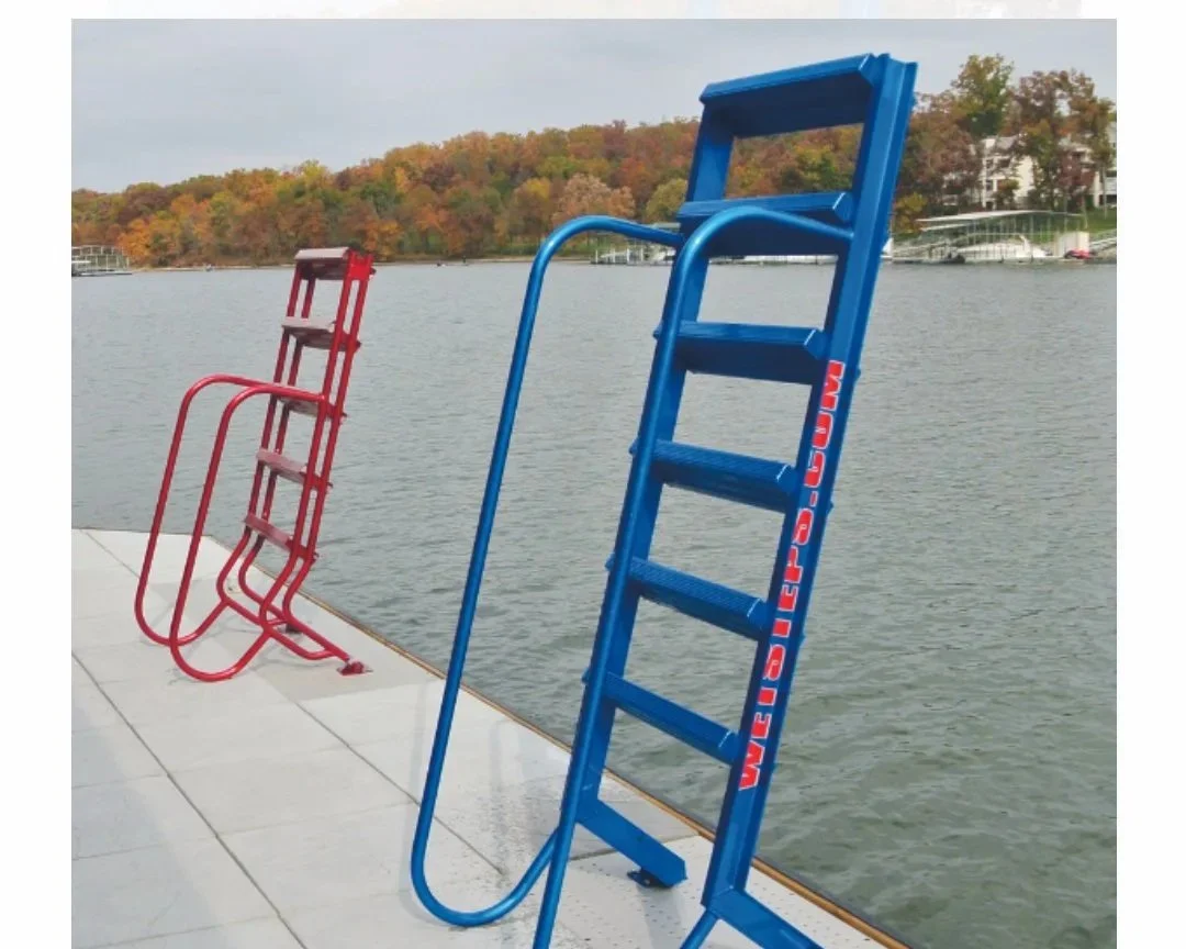 Two foldable ladders, one blue and one red, placed by a lakeside dock with trees and houses in the background.