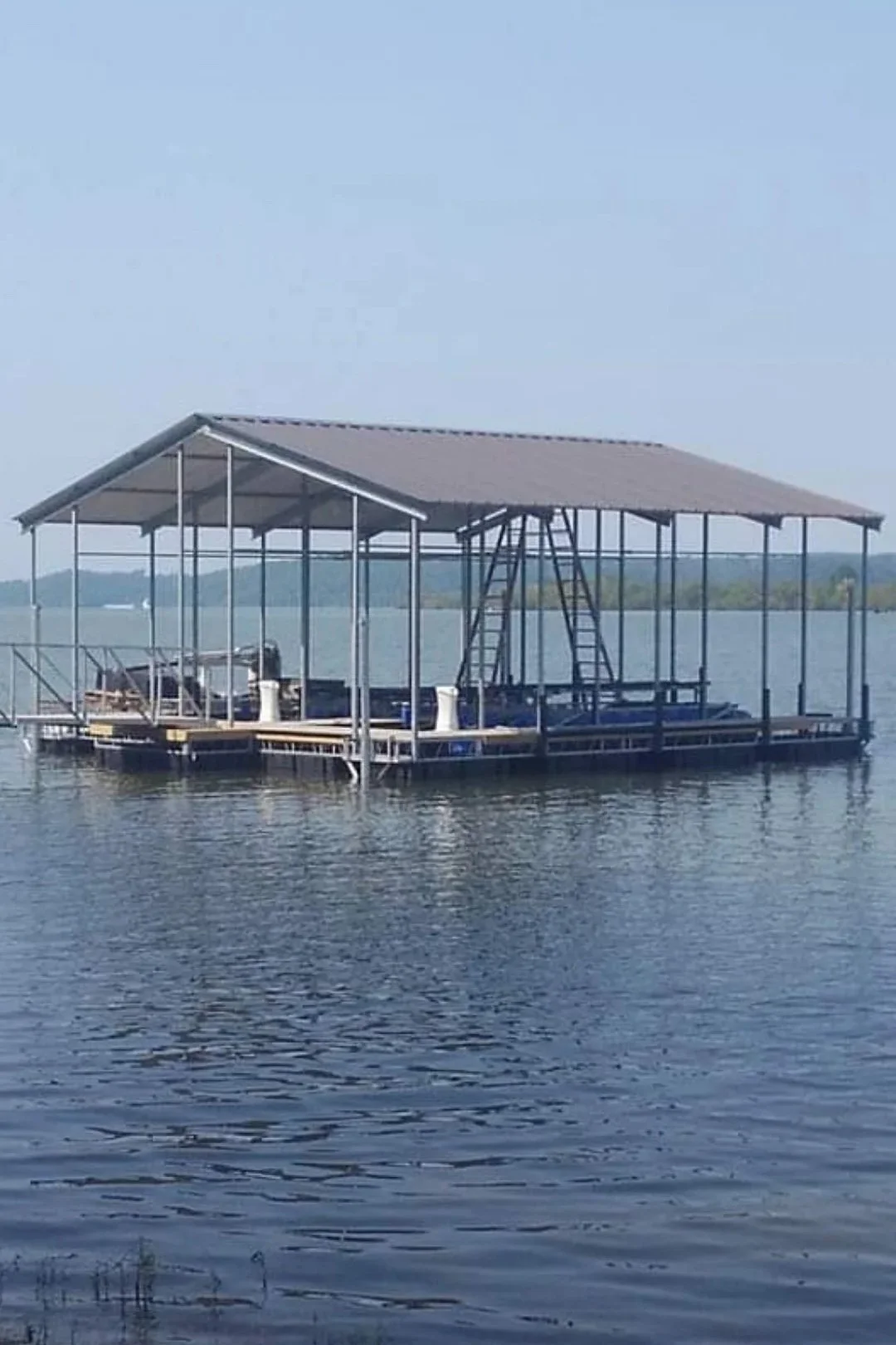 A floating boat dock with a roof on water, with ladders and boating equipment, under a clear blue sky.