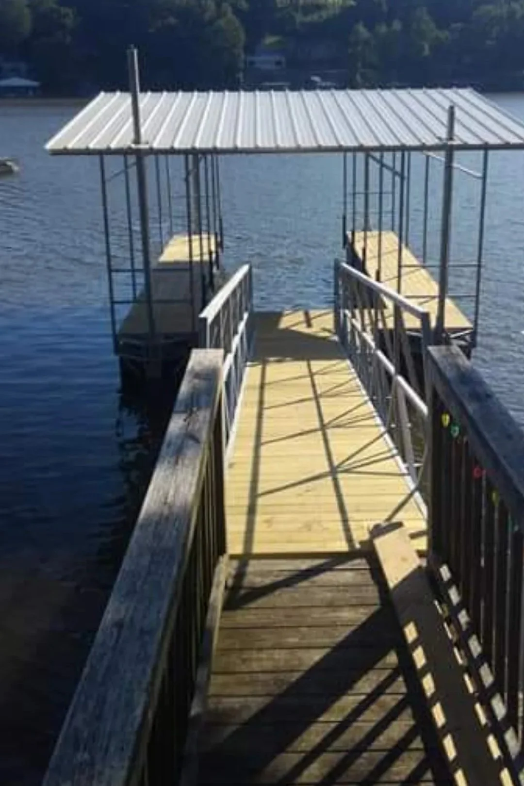 A small dock with a metal roof extends over a body of water, featuring two benches at the end and a walkway with railings.