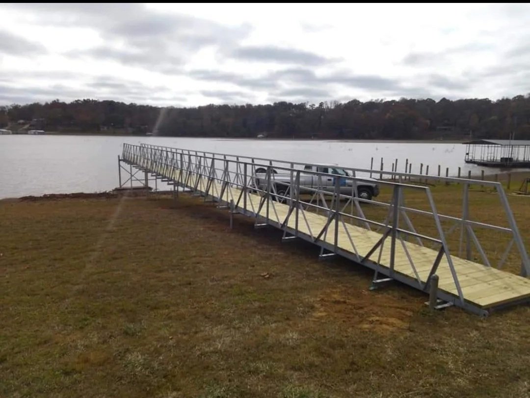 A metal dock extending into a lake or river, with a pickup truck parked nearby on the grass.
