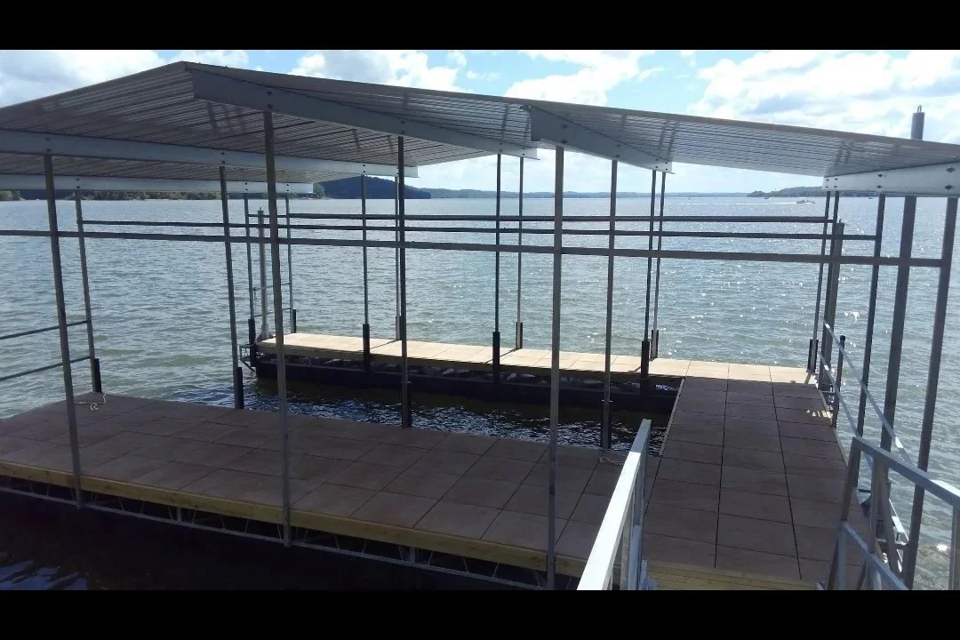 Dock with metal roof and safety rails on a body of water, with land and trees in the distance under partly cloudy skies.