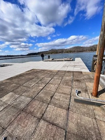 A dock extending over a lake with two people walking in the distance under a partly cloudy sky.