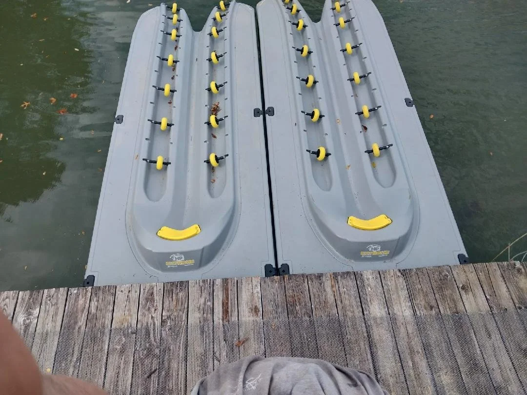 A floating dock with two water skiers or wakeboard ramps, each with multiple yellow ski or wakeboard holders, attached to the edge of a wooden dock on a body of water.