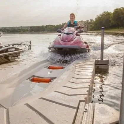 Person riding a pink jet ski on the water near a wooden dock with boats in the background.