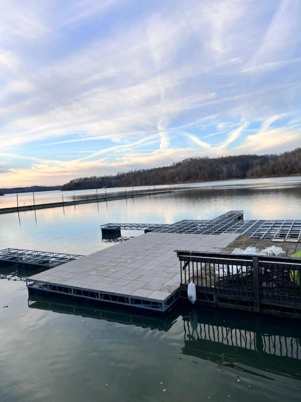 Floating dock on a calm lake with a cloudy sky and distant hilly shoreline.