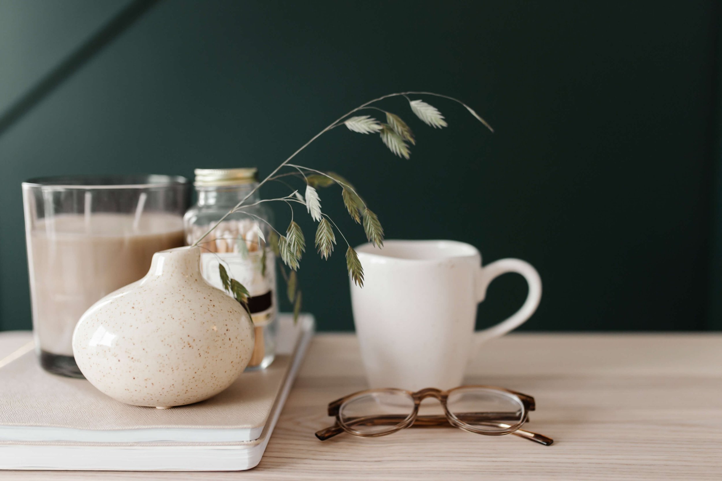 glasses coffee mug and candle on desk by green wall