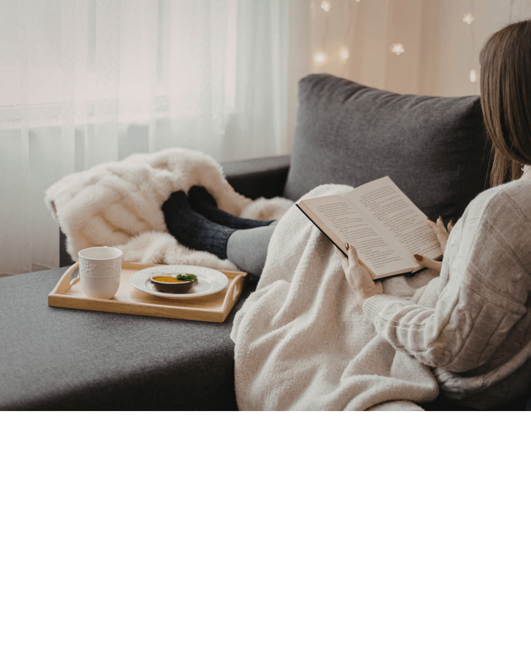 Woman recovering on couch with blanket, cup of tea and a book.