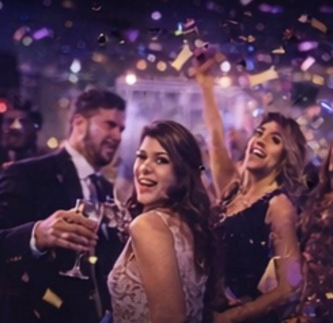 People celebrating at a party with confetti, smiling and holding drinks.