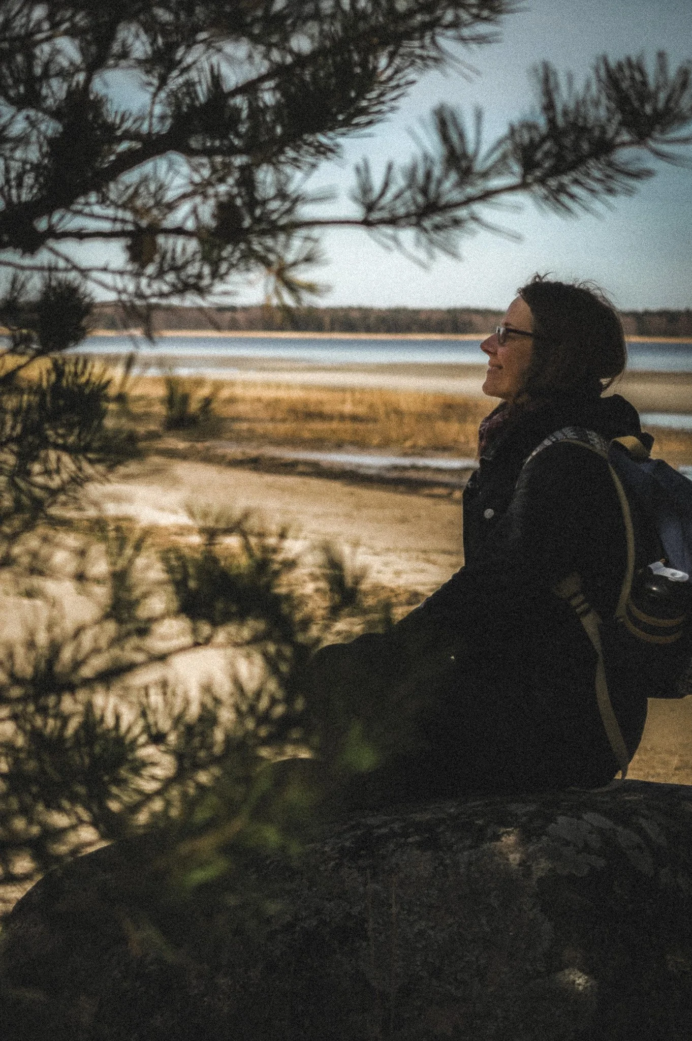 Silvia sitting on a rock on a beach in Estonia, smiling.