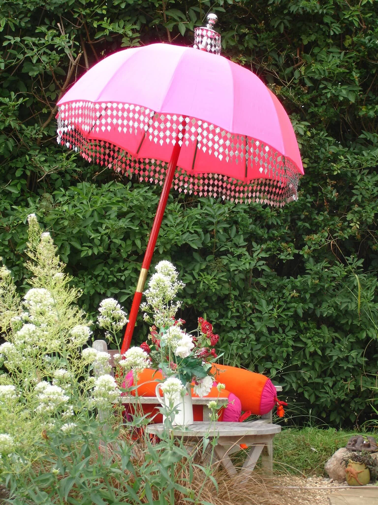 Pink Raj umbrella with decorative fringing displayed in an English garden made for The Indian Garden Company