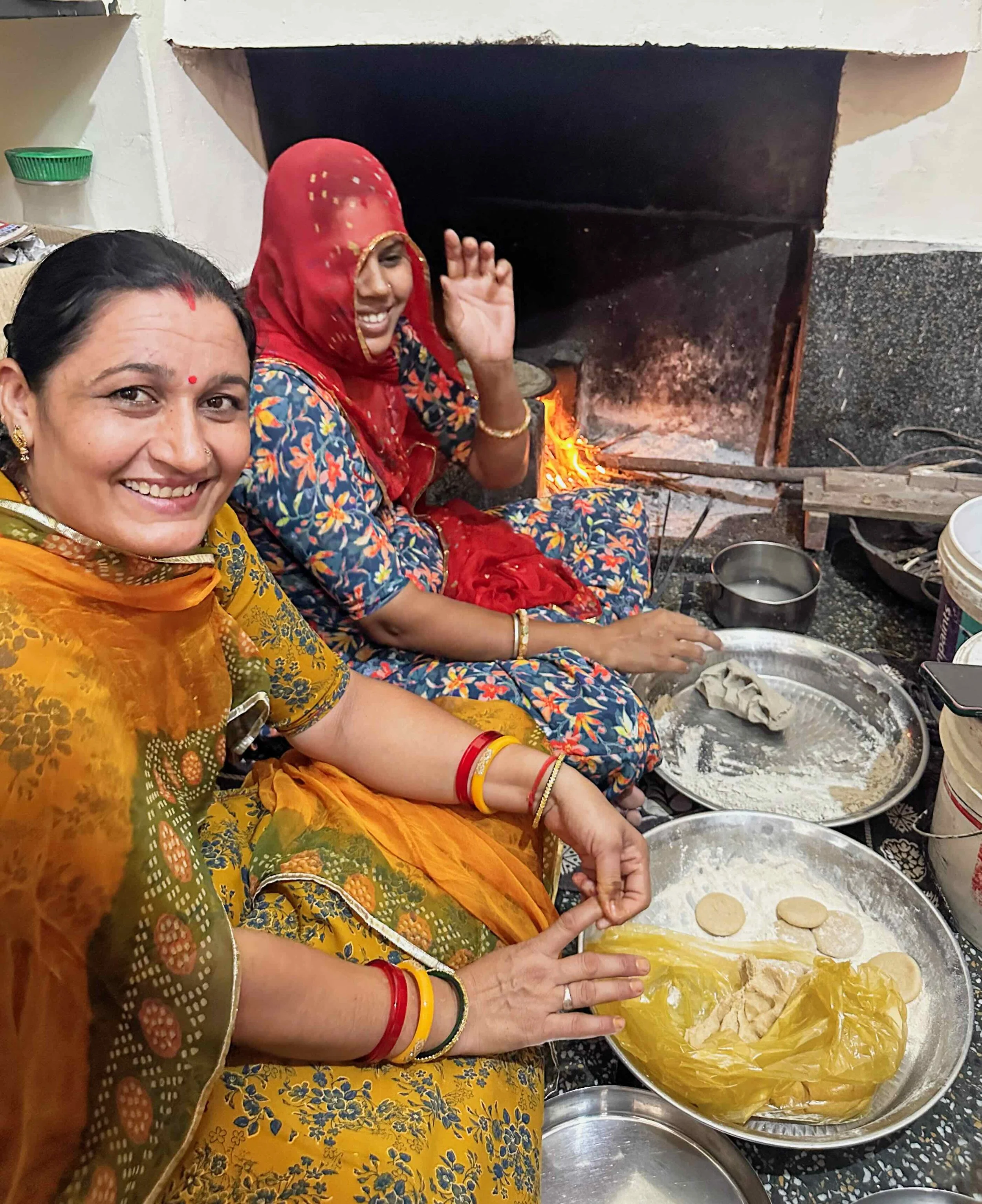 Two women in traditional Rajasthani dress cooking chapati on an open fire in Ruma Devi’s kitchen, Barmer, Rajasthan, Diwali 2025