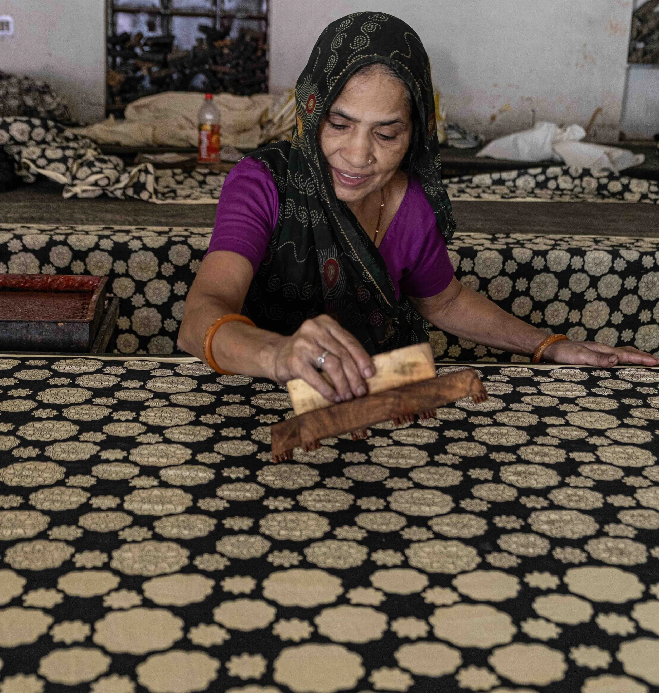 Woman applying dabu mud resist paste with a wooden block in a natural dye workshop in Bagru, Rajasthan